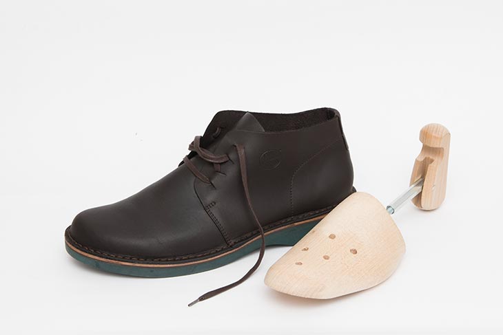 ein Schuh aus braunem Leder und grüner Sohle und ein Schuhspanner aus Holz vor weißem Hintergrund