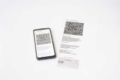Smartphone mit QR-Code im Display, daneben der Ausdruck dieses Bildschirms